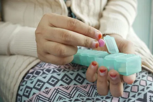 A woman's hands is holding a pill box in her lap taking a tablet out, she is struggling with painkiller addiction