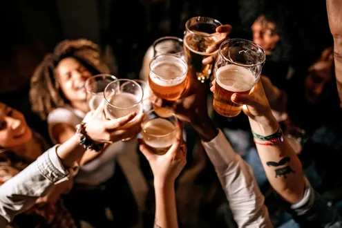 A group of people in a circle raise their glasses filled with alcohol in celebration